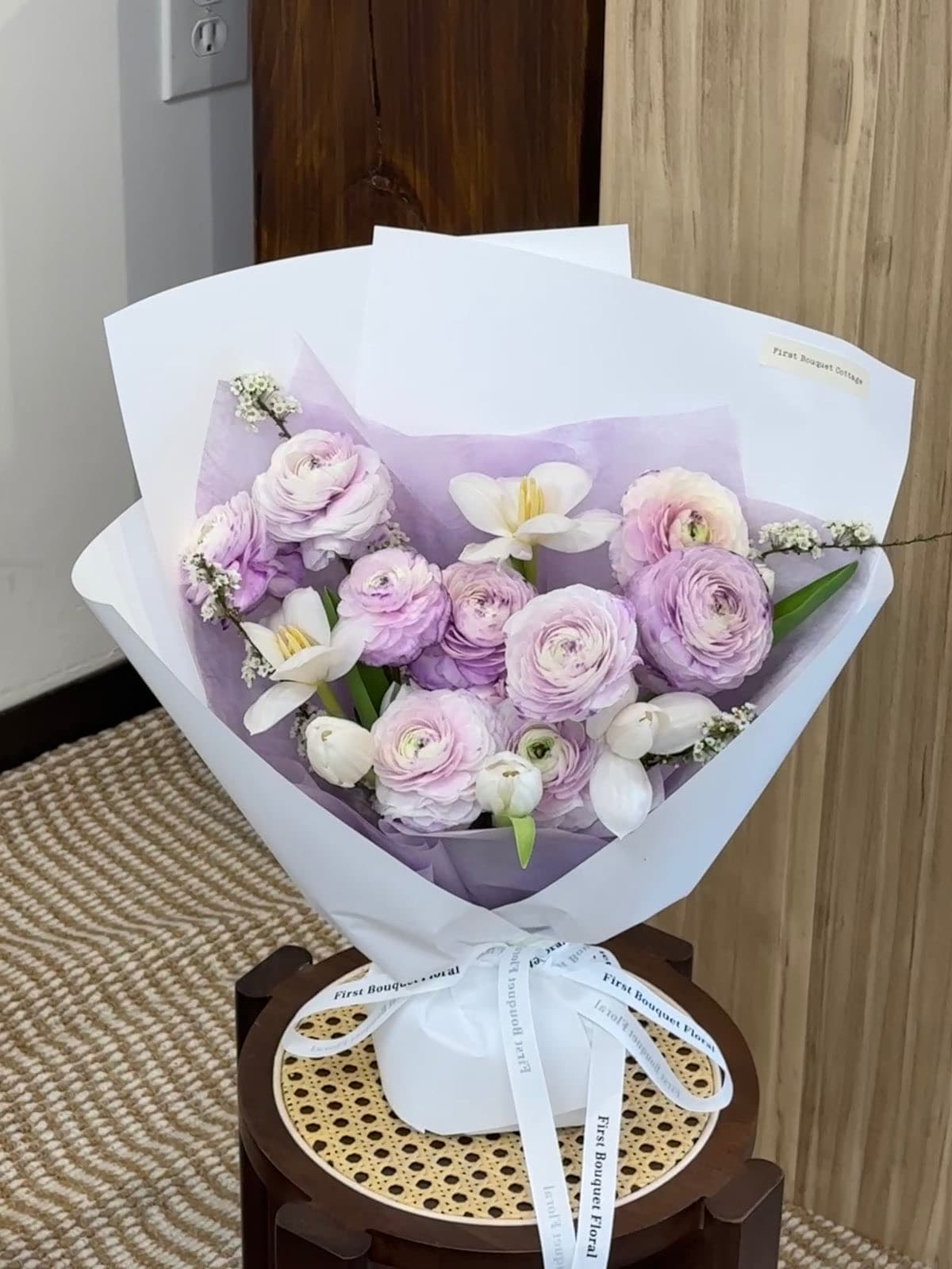 Lilac lisianthus and white orchids in lavender wrapping, tied with white ribbon.